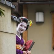 Geisha looking around corner and smiling at the camera