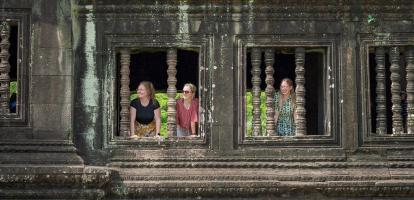 Three women smile behind stone windows in the ruins of Angkor Wat in Cambodia's Siem Reap