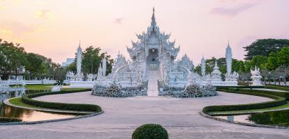 Sunset colors the garden and beautiful whites of Wat Rong Khun, Chiang Rai's famous white temple in northern Thailand