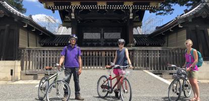 Three cyclists smile in front of a shrine in Kyoto, Japan
