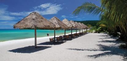 White-sand beach lined with straw-thatched umbrellas next to azure waters in Cambodia's coast.