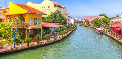 Ferry in Malacca's river next to bright and colorful buildings in Malaysia