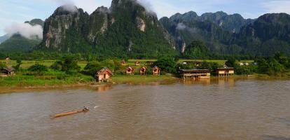 Riverside view of sunset in Vang Vieng, with small huts surrounded by mountains