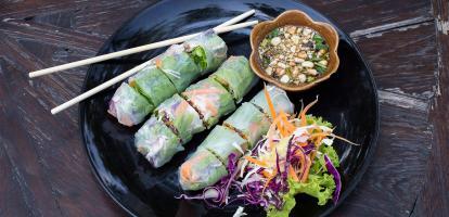Delicious Vietnamese rice paper spring rolls sit in a dish on a wooden table