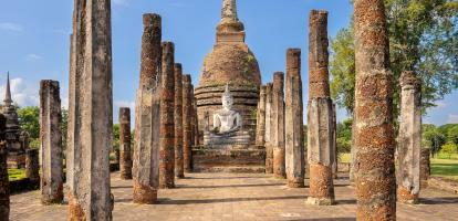 White buddha sits among stone pillars in Wat Sa Si temple in Sukhothai, Thailand