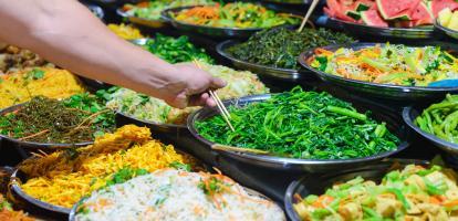 Person grabs food from a buffet filled with vegetables using chopsticks in Luang Prabang, Laos