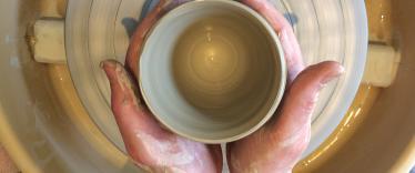 Hands are shaping clay on a pottery wheel, cast in a warm light