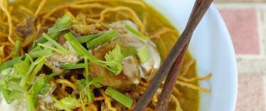 Bowl of curry noodles with chopsticks and lime to garnish