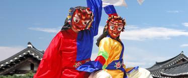 Two traditional folk dancers wearing masks dance in front of hanok houses in South Korea