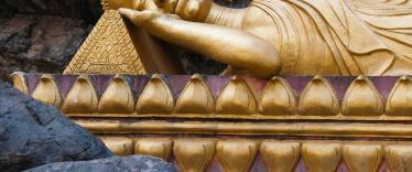 Reclining gold gilt buddha on purple platform surrounded by craggy rocks