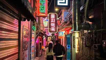 People walking away in a narrow, neon-lit alleyway with Korean signs