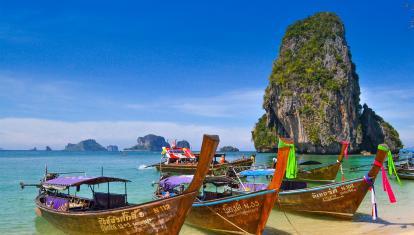 Boats parked in an azure beach surrounded by karst rock formations in Krabi, Thailand