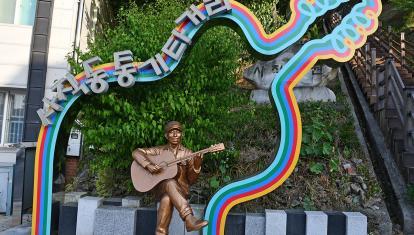 Brass statue of a man playing his guitar, sitting under a bigger guitar frame