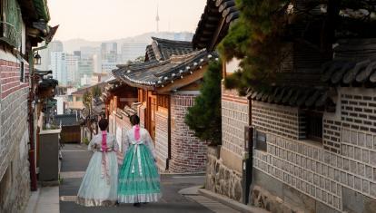 Back of two women wearing hanbok walking through the traditional style houses of Bukchon Hanok Village in Seoul, South Korea.