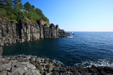 Rocky shoreline of Jeju Island with yacht in the sea in the background