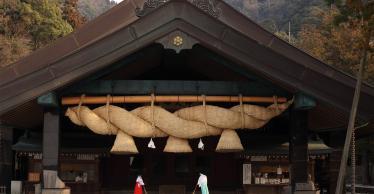 Two ladies in traditional dress sweeping front of wooden shrine