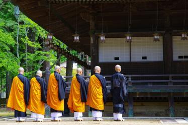 Monks in orange robes lined up to pray outside wooden temple