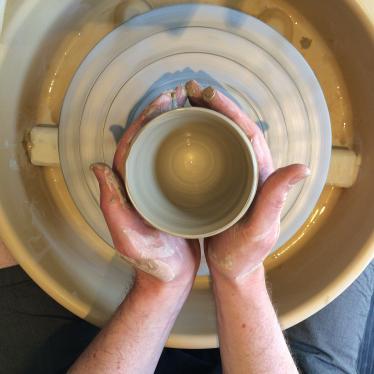 Hands are shaping clay on a pottery wheel, cast in a warm light