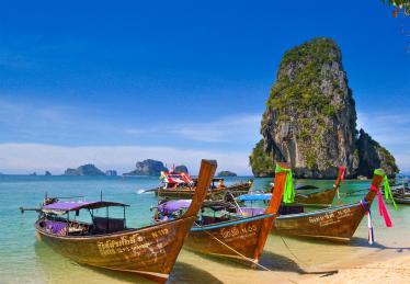 Boats parked in an azure beach surrounded by karst rock formations in Krabi, Thailand